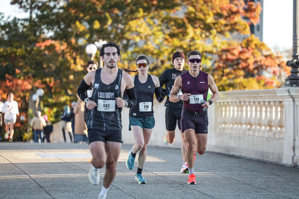 Hank running with a race pack beside a white bridge railing and autumn trees.