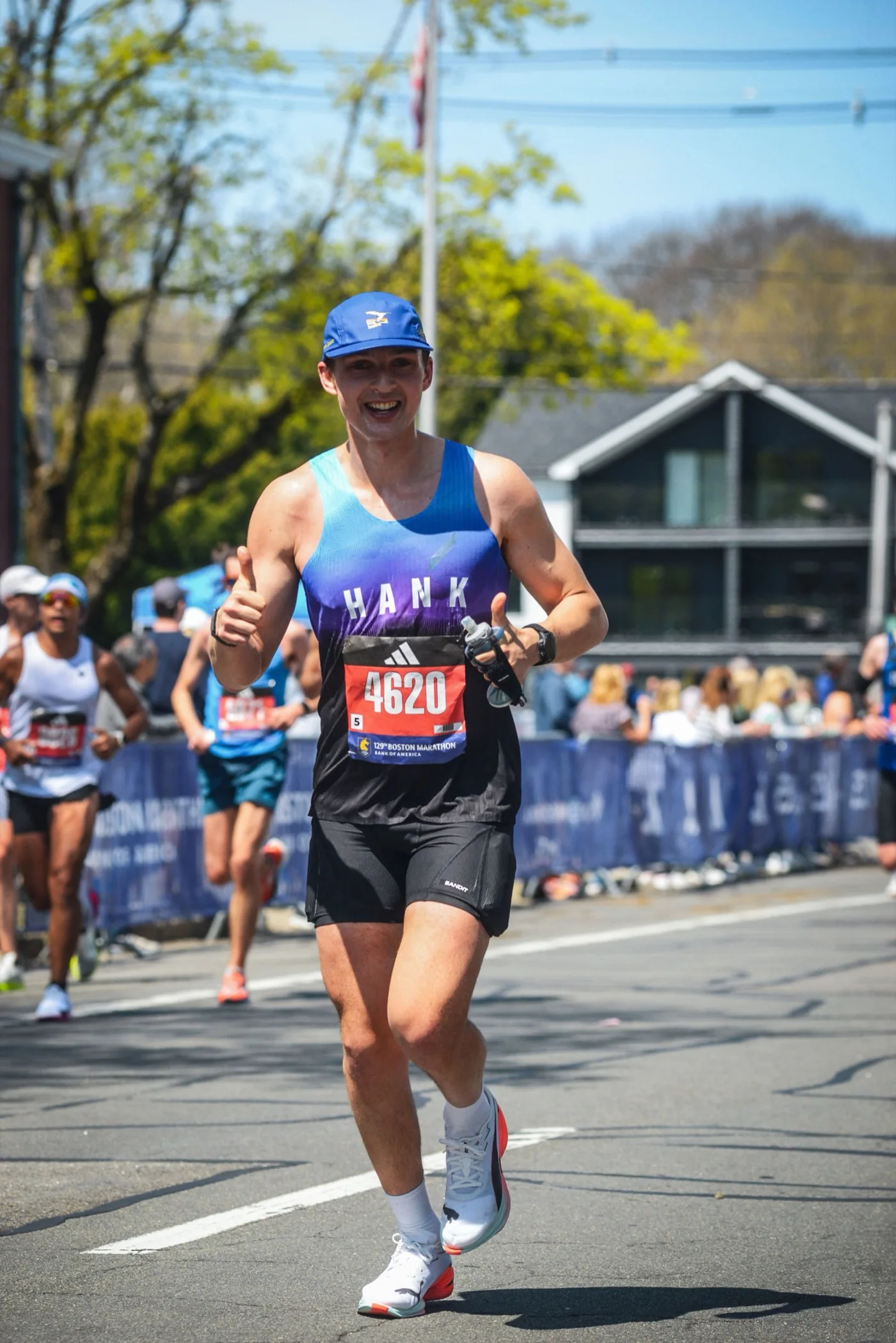 Hank smiling and giving a thumbs-up during a race, wearing a blue cap and HANK singlet.